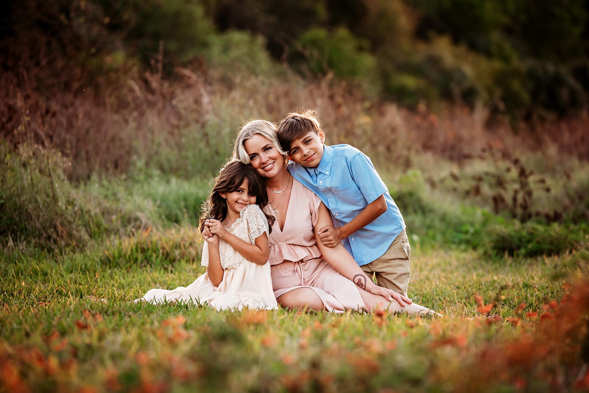 Mom and her two children sit in a field in Fort Myers Fl for their family photography session wearing shades of pink and blue