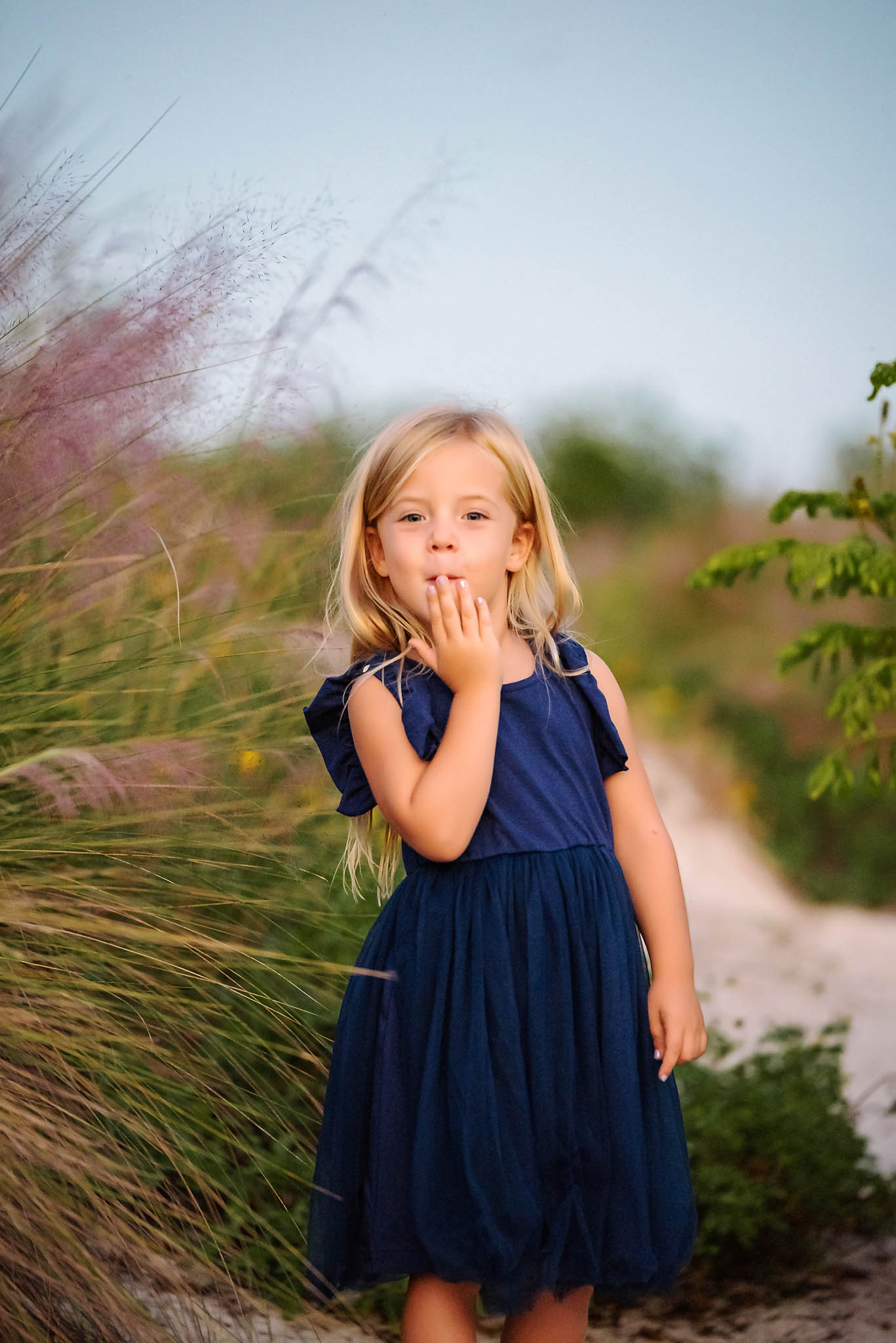 LIttle girl in blue dress blows a kiss towards the camera