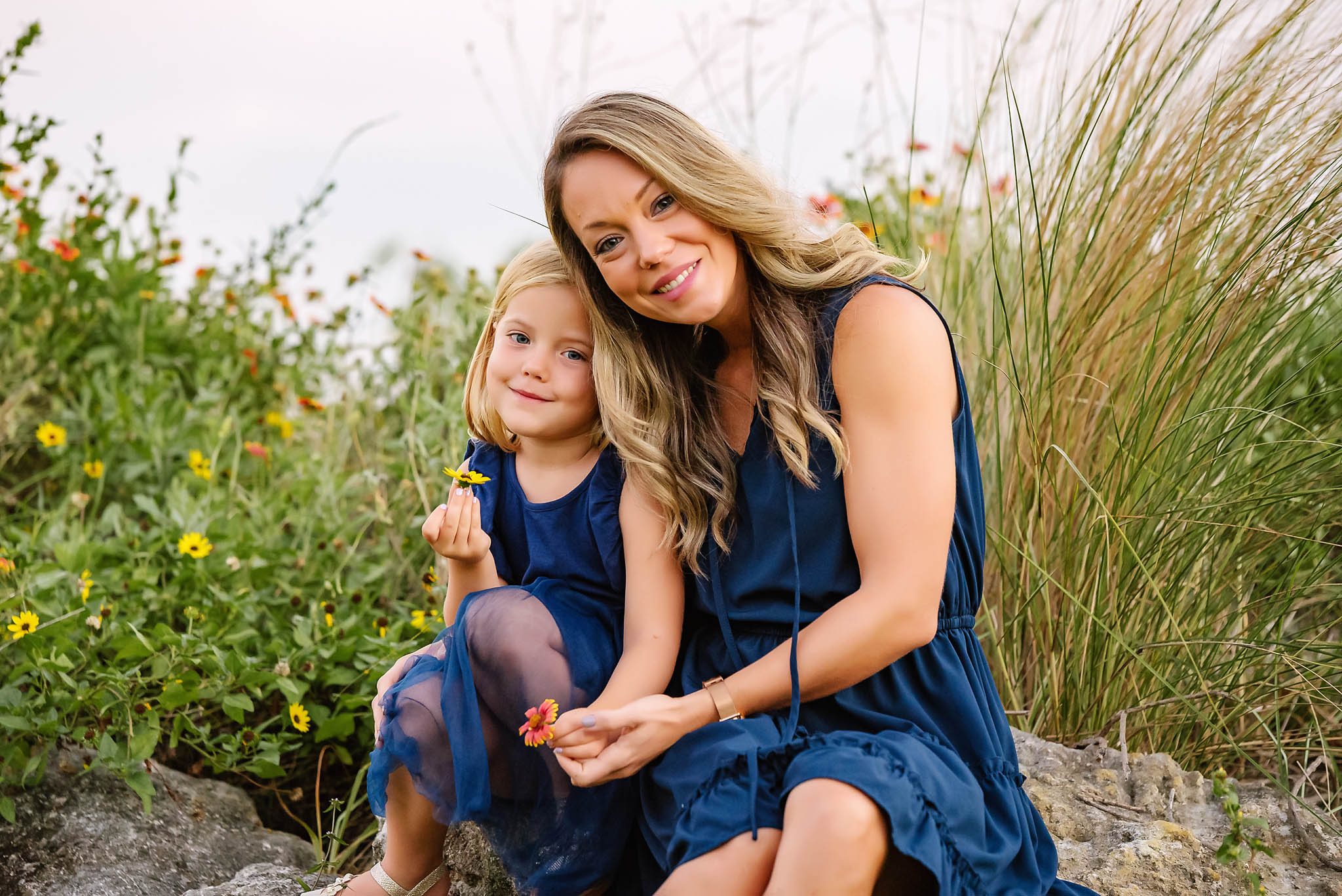 Sweet mom and her little one hold a flower while sitting on a rock in tall grass
