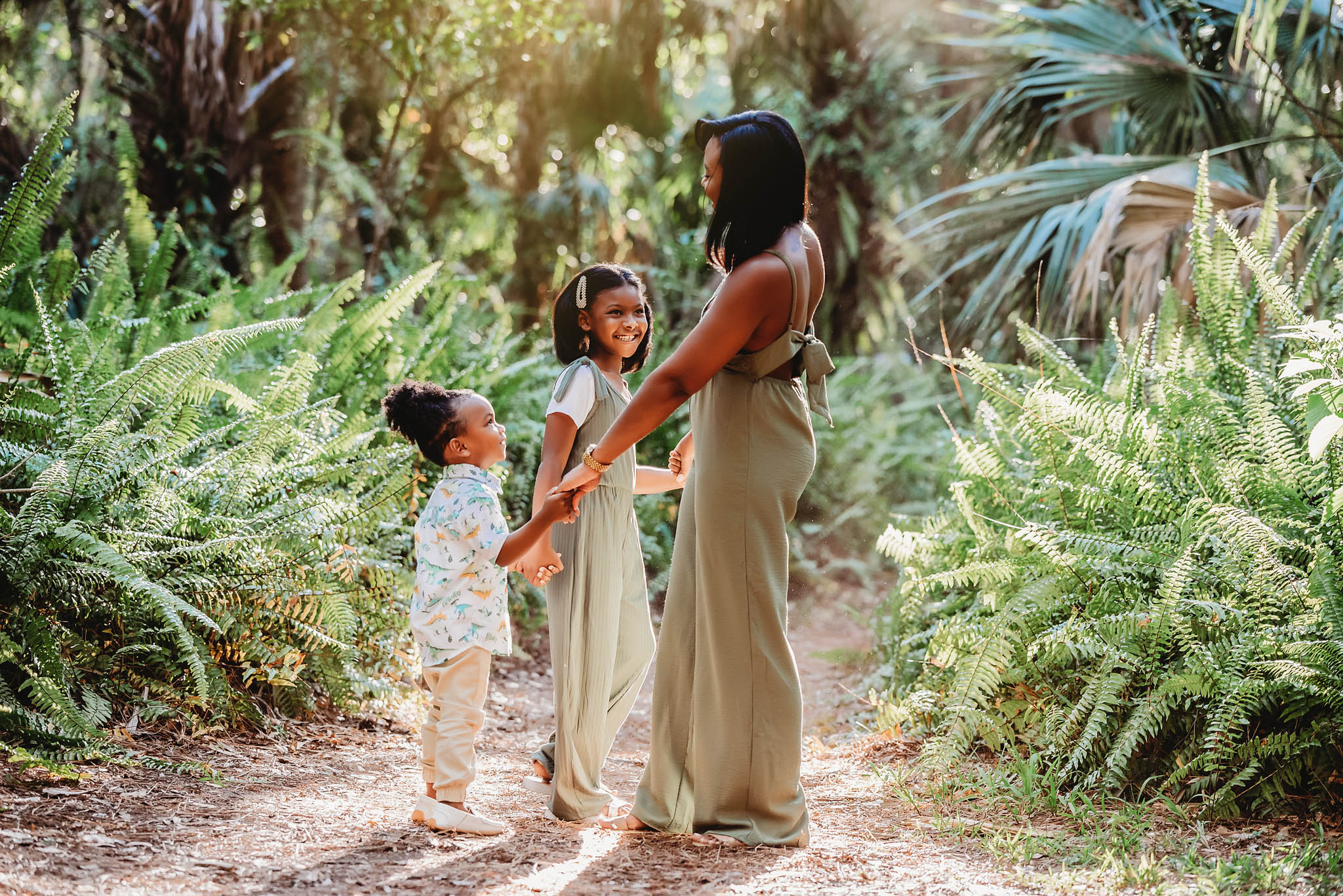 Mom and her children dancing together on trail in Fort Myers, Florida, Surrounded by lush ferns.
