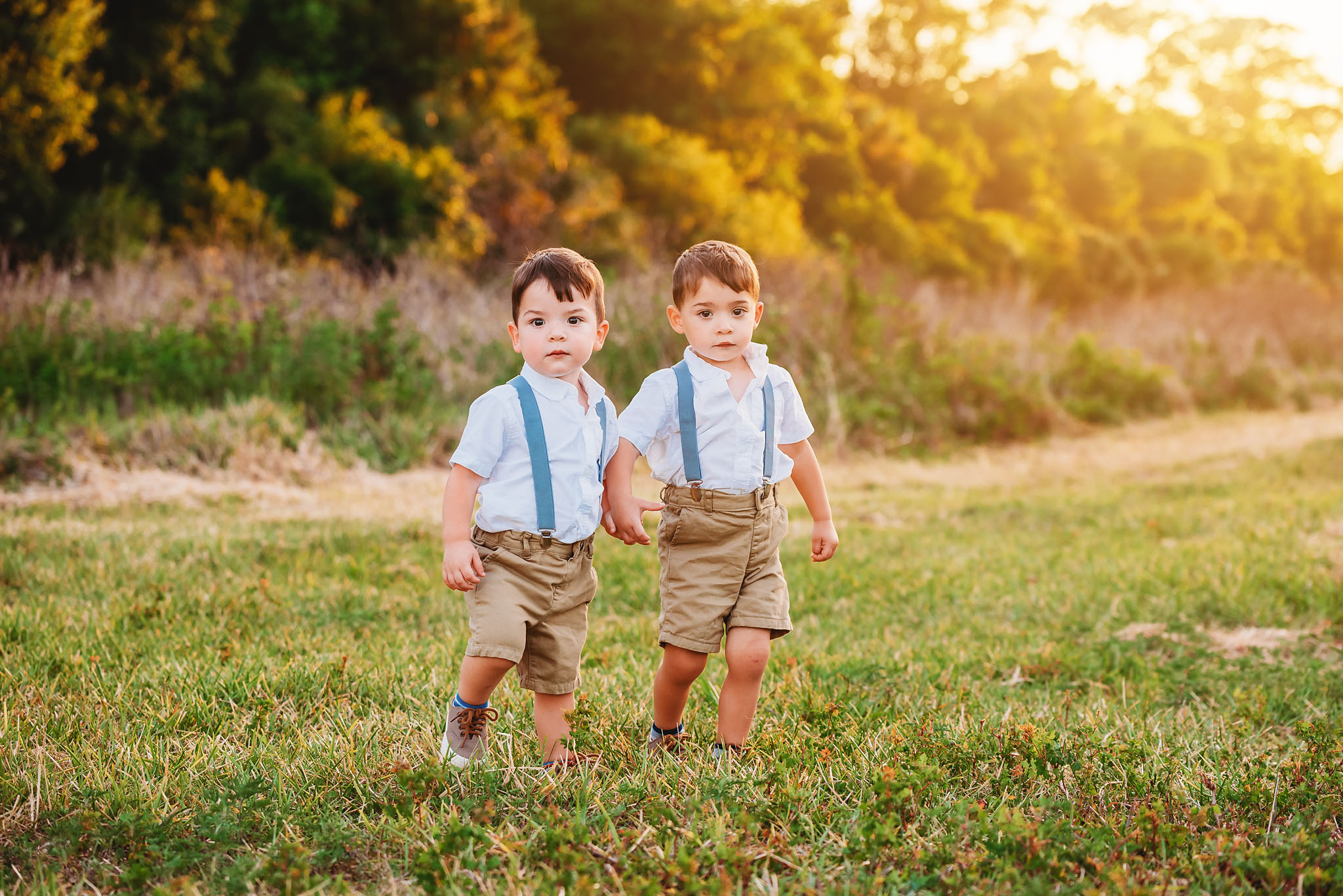two sweet twin boys in blue suspenders holding hands in fort myers during their family photoshoot